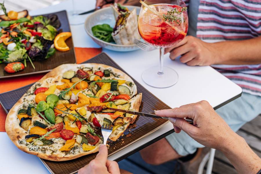 Vegetarischer Flammkuchen wird von Person angeschnitten